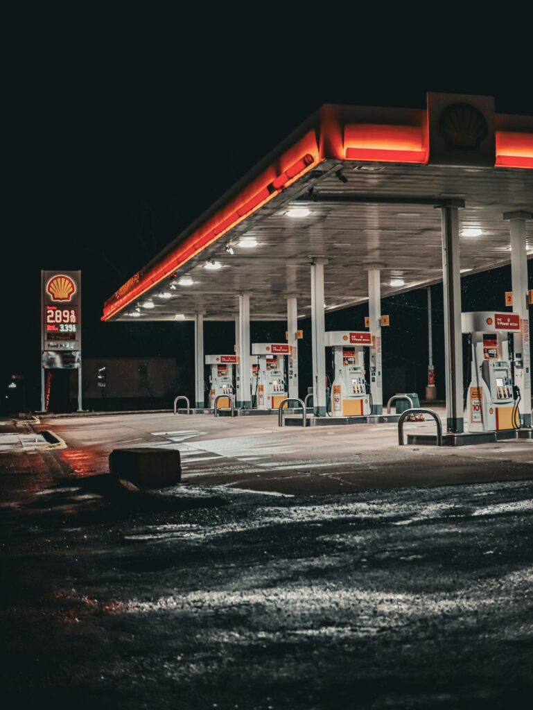 An empty gas station illuminated at night, creating a moody atmosphere with reflections on the wet pavement.